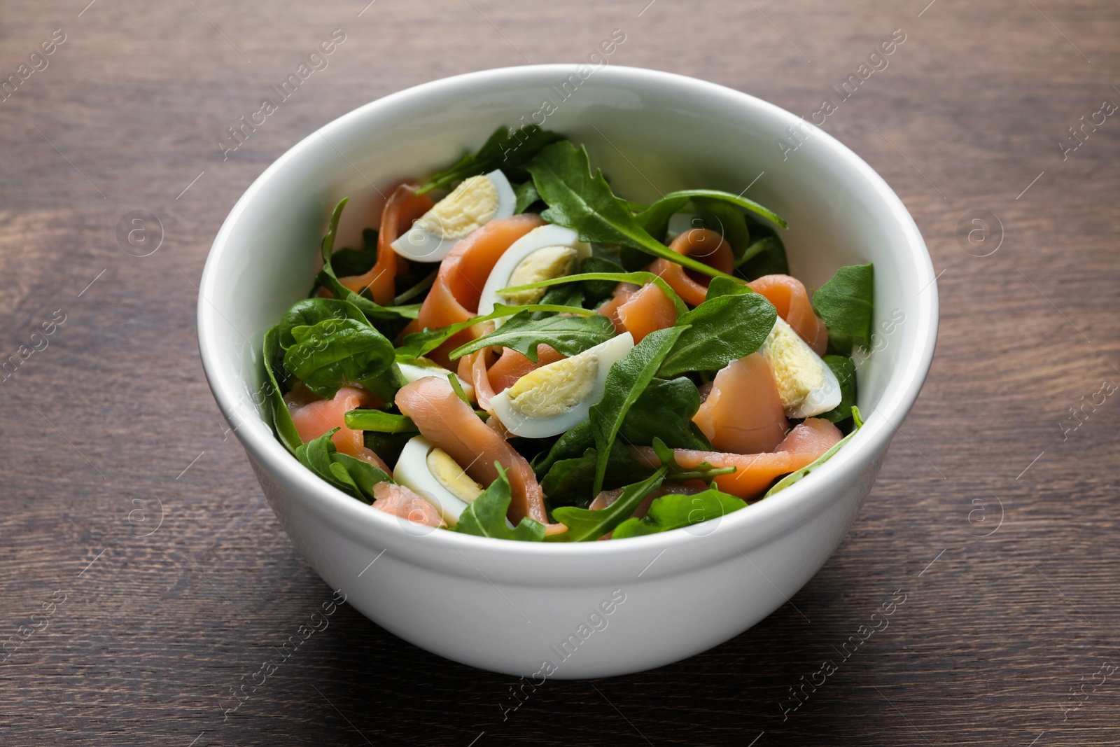 Photo of Delicious salad with boiled eggs, salmon and arugula on wooden table, closeup