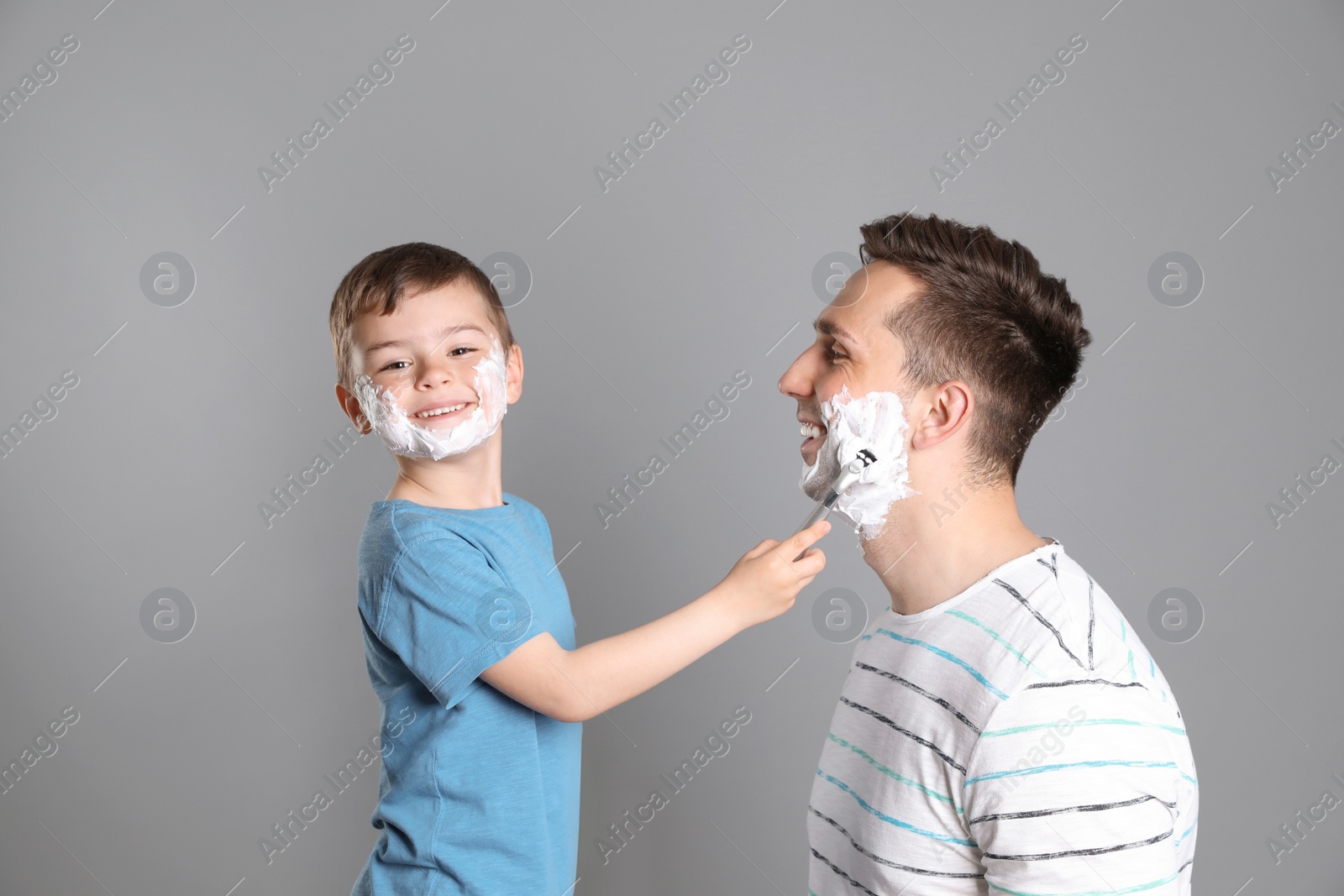 Photo of Little son shaving his father on color background