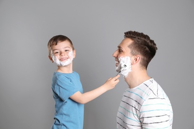 Photo of Little son shaving his father on color background