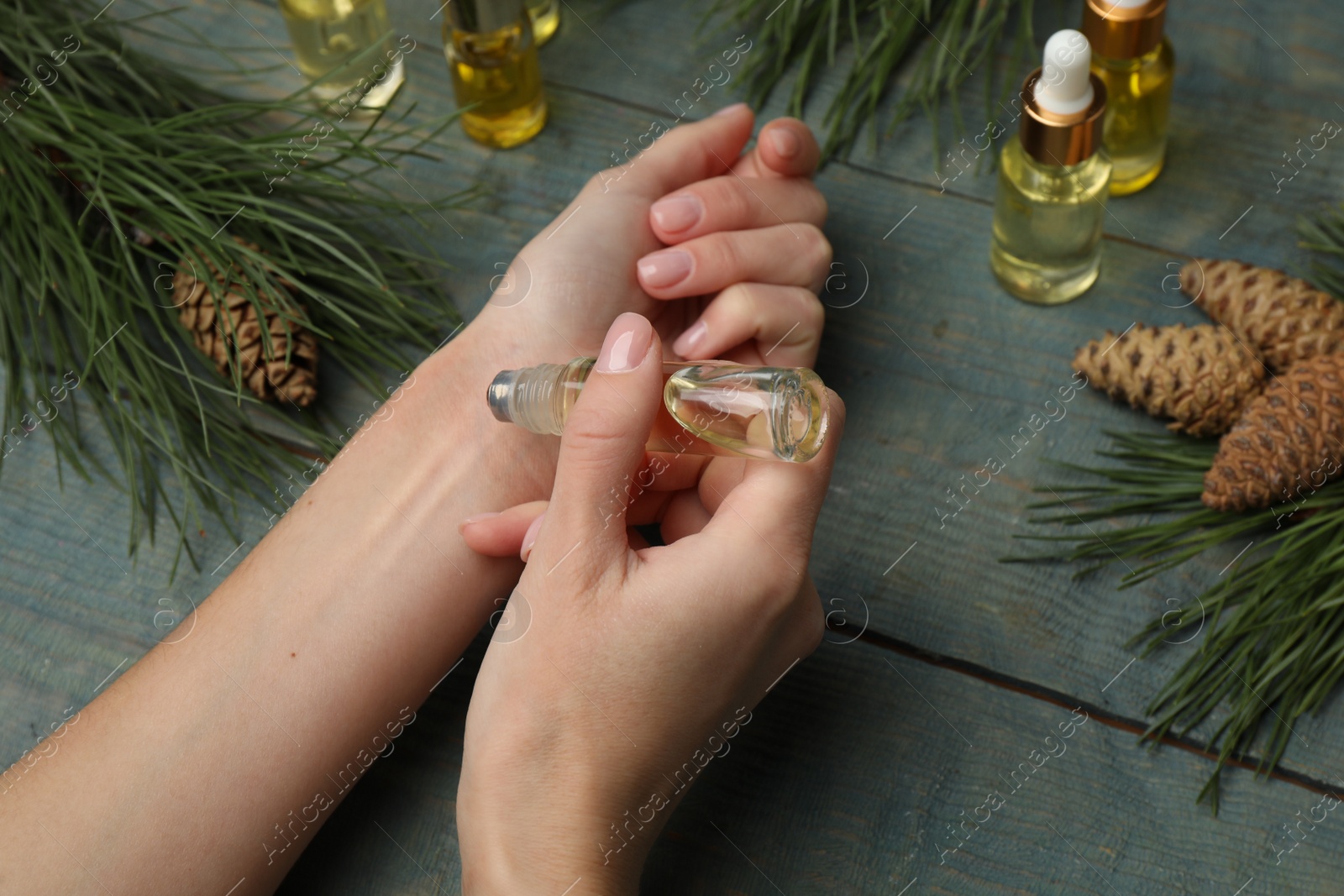 Photo of Woman applying pine essential oil on wrist at light blue wooden table, closeup
