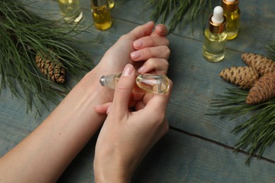 Woman applying pine essential oil on wrist at light blue wooden table, closeup