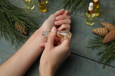 Photo of Woman applying pine essential oil on wrist at light blue wooden table, closeup