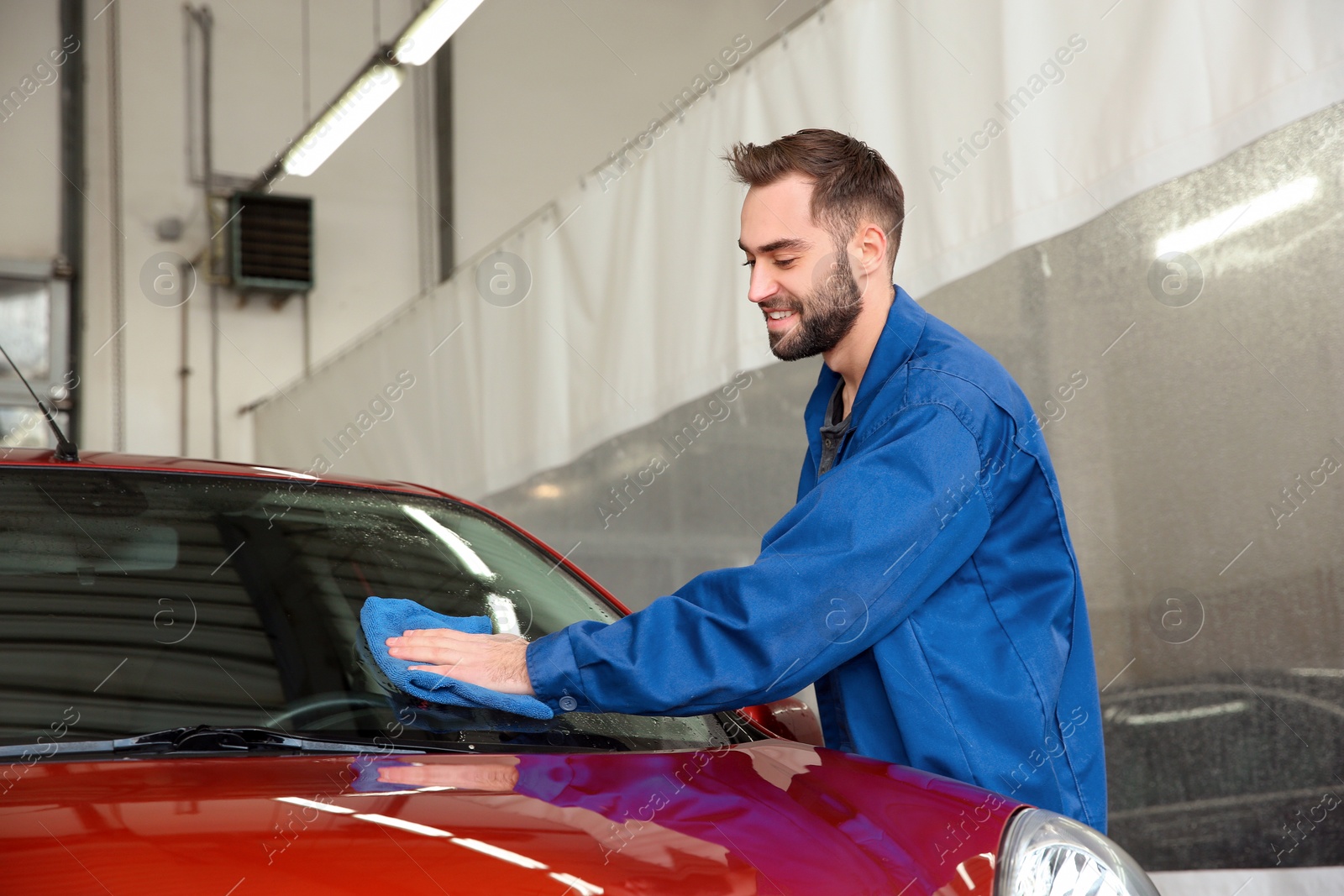 Photo of Worker cleaning automobile windshield with rag at car wash