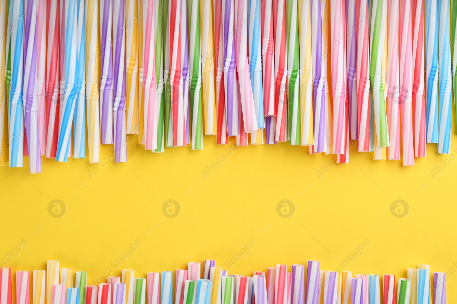 Photo of Heap of colorful plastic drinking straws on yellow background, flat lay. Space for text