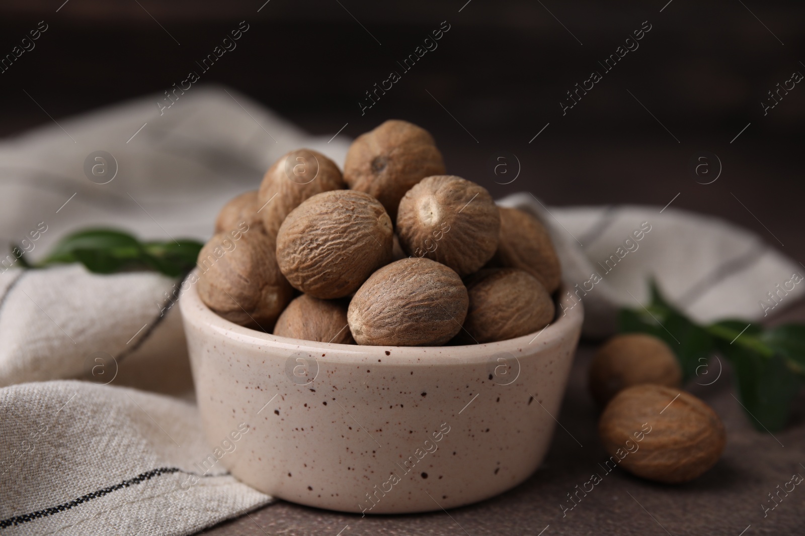 Photo of Whole nutmegs in bowl on brown table, closeup