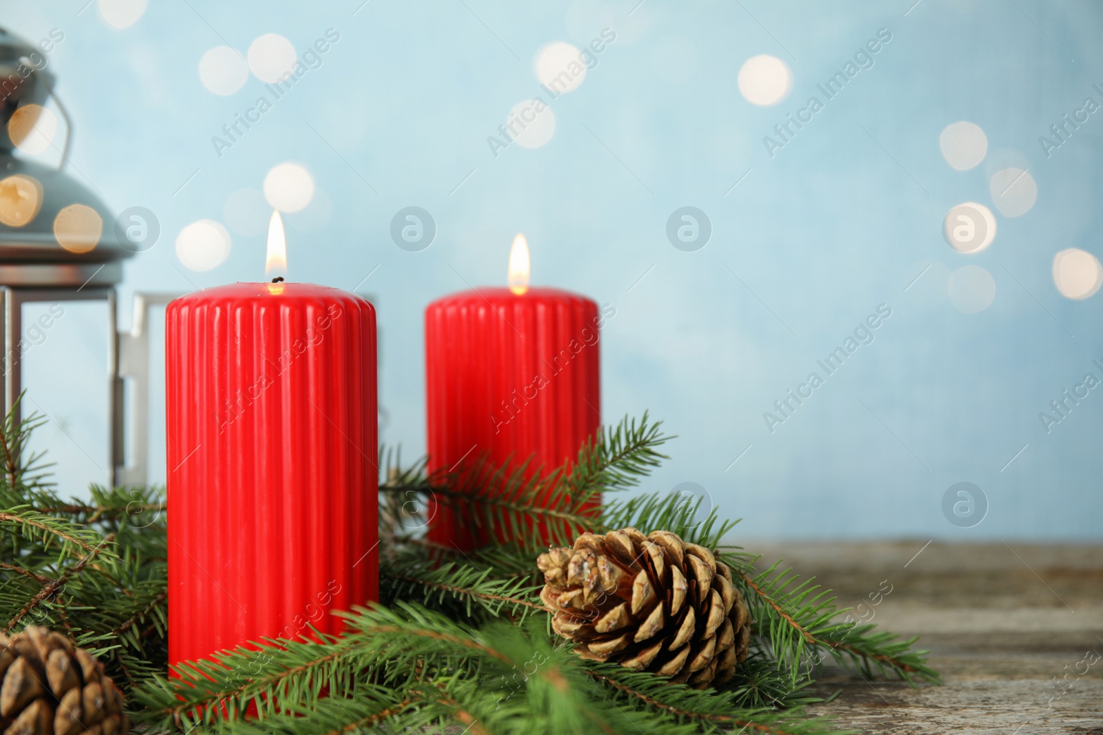 Photo of Burning candles and fir branches on wooden table against light blue background, bokeh effect. Space for text