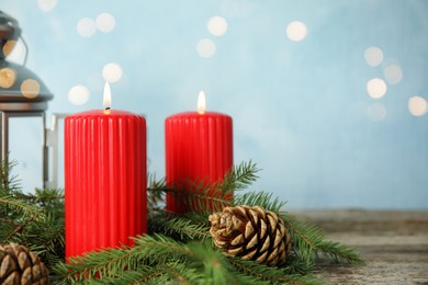 Photo of Burning candles and fir branches on wooden table against light blue background, bokeh effect. Space for text