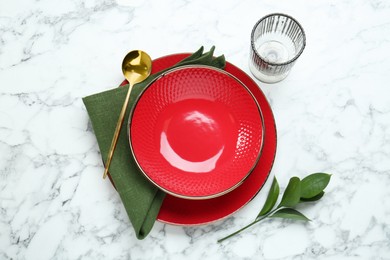 Stylish ceramic plates, spoon, glass and floral decor on white marble table, top view