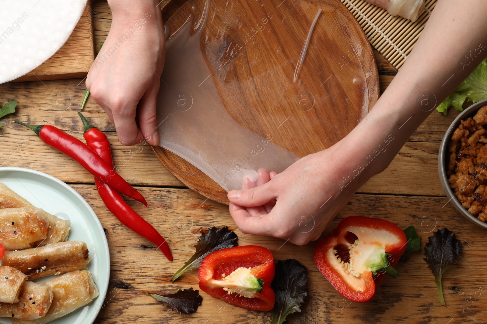 Photo of Woman making tasty spring roll at wooden table, top view