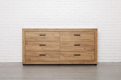 Photo of Wooden chest of drawers near white brick wall. Interior design