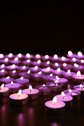 Beautiful burning violet candles on black background. Funeral attributes