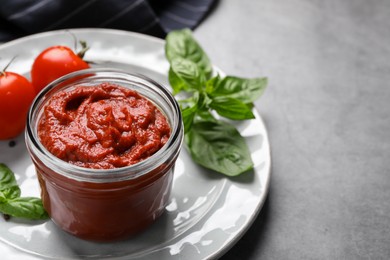 Jar of tasty tomato paste on gray table. Space for text