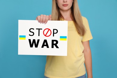 Image of Woman holding poster with words Stop War and Ukrainian flags on light blue background, closeup