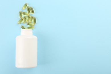 Photo of Bottle and vitamin capsules on light blue background, top view. Space for text