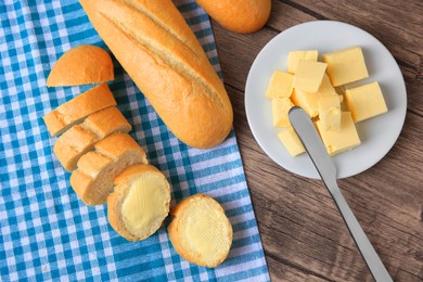 Photo of Tasty cut baguette with fresh butter on wooden table, flat lay