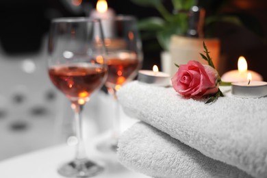 Rose and burning candle on towel near glasses of wine, closeup. Romantic bath