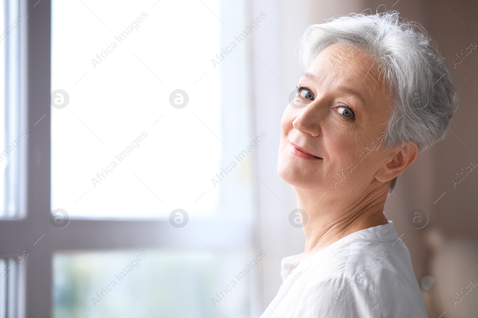 Photo of Happy mature woman near window indoors, space for text. Smart aging