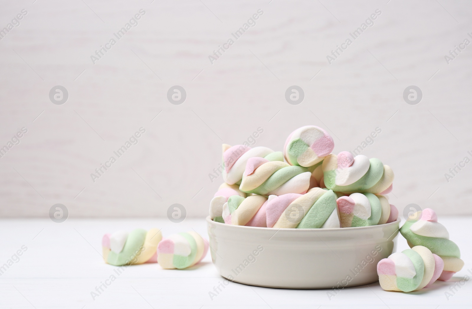 Photo of Bowl with colorful marshmallows on white table. Space for text