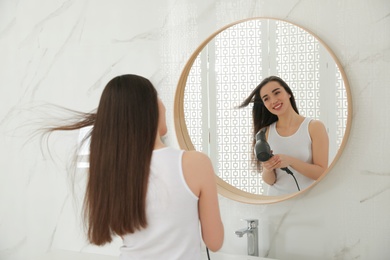 Beautiful young woman using hairdryer in bathroom