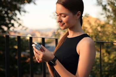 Photo of Attractive happy woman checking pulse with blood pressure monitor on finger after training in park