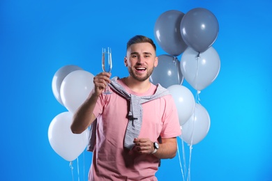 Portrait of happy man with champagne in glass and party balloons on color background