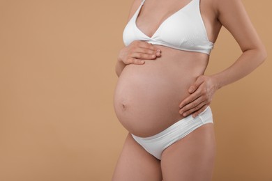 Photo of Pregnant woman in stylish comfortable underwear on beige background, closeup. Space for text