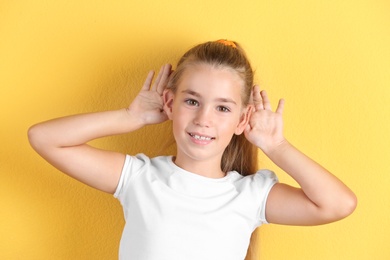 Cute little girl with hearing problem on color background