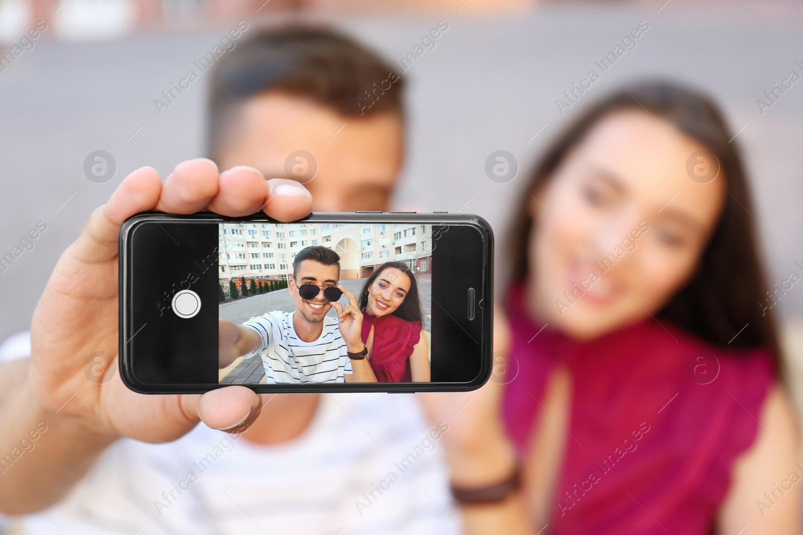 Photo of Young couple taking selfie outdoors, focus on smartphone