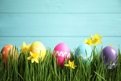 Colorful Easter eggs and narcissus flowers in green grass against light blue background. Space for text