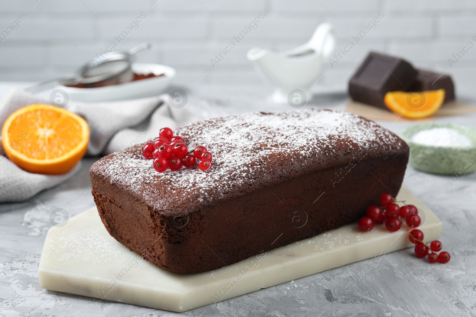 Photo of Tasty chocolate sponge cake with powdered sugar and currant on light grey textured table, closeup