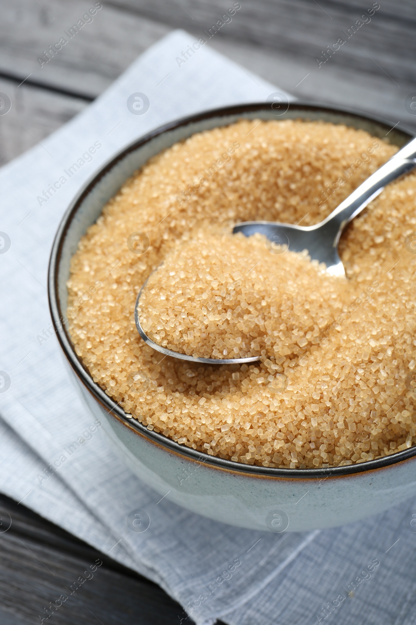 Photo of Brown sugar in bowl and spoon on black wooden table, closeup