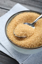 Brown sugar in bowl and spoon on black wooden table, closeup