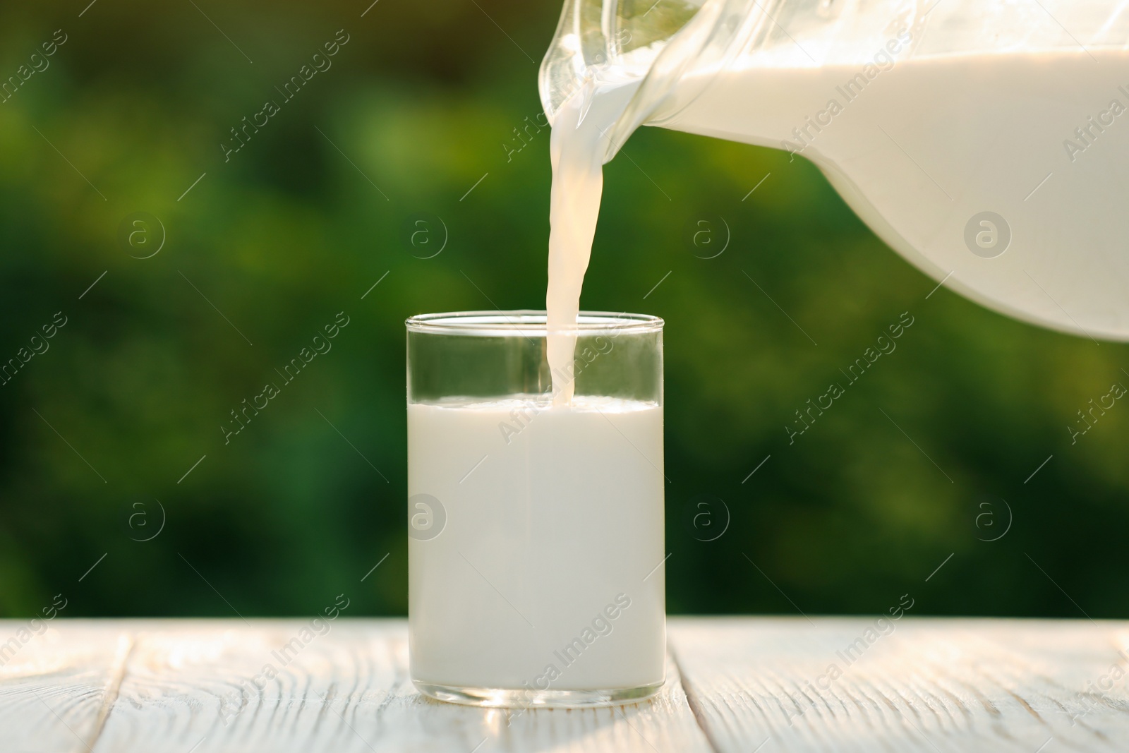 Photo of Pouring tasty fresh milk from jug into glass on white wooden table, closeup
