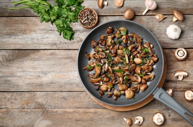 Photo of Frying pan of mushrooms on wooden background, flat lay with space for text