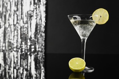 Photo of Martini cocktail with lemon slice on black and silver background, space for text