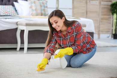 Photo of Young woman cleaning carpet with brush in bedroom