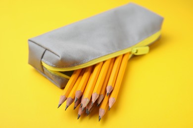 Photo of Many sharp pencils in pencil case on yellow background