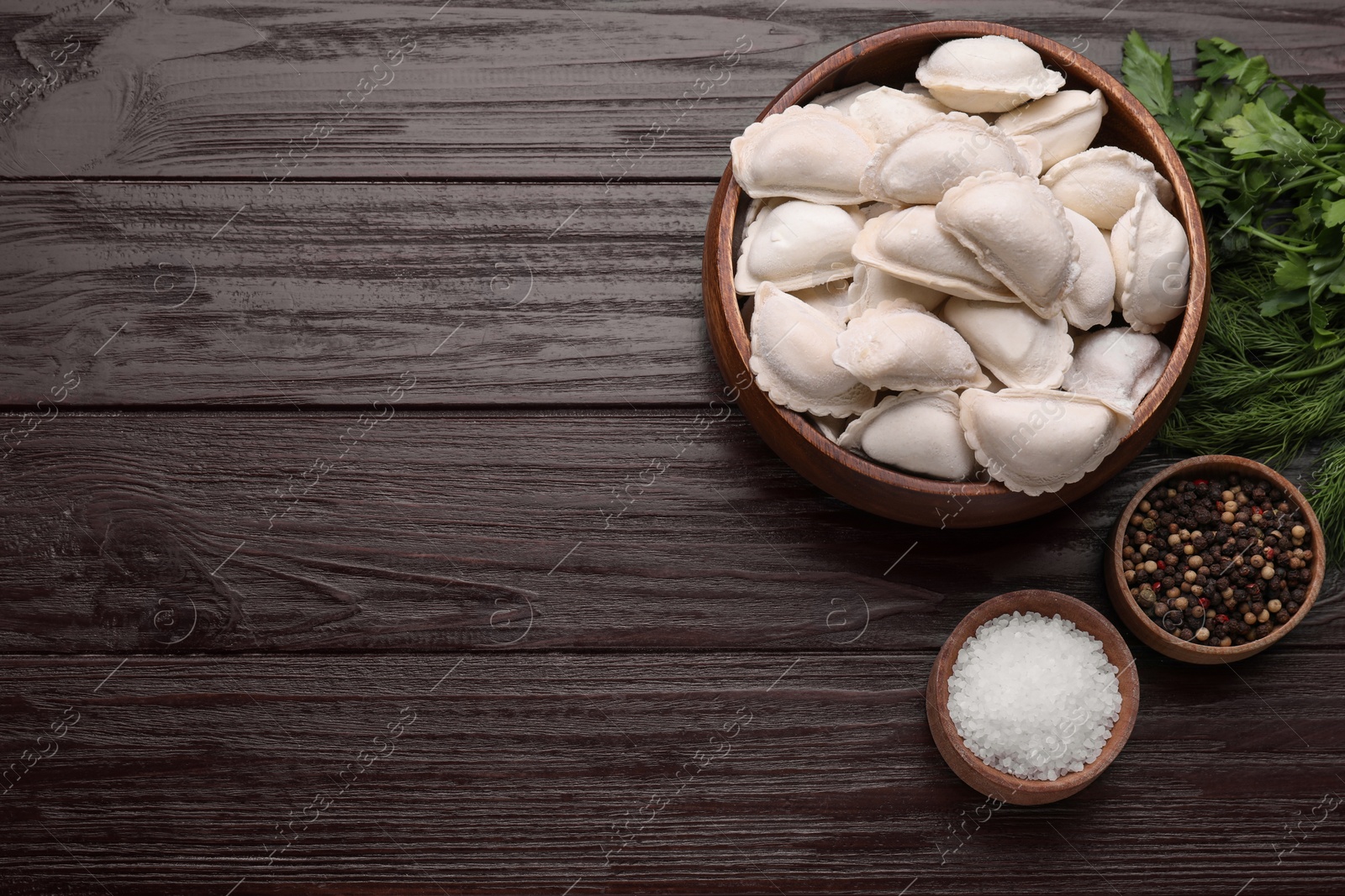 Photo of Raw dumplings (varenyky) and ingredients on brown wooden table, flat lay. Space for text