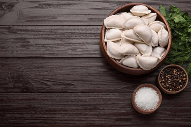 Raw dumplings (varenyky) and ingredients on brown wooden table, flat lay. Space for text