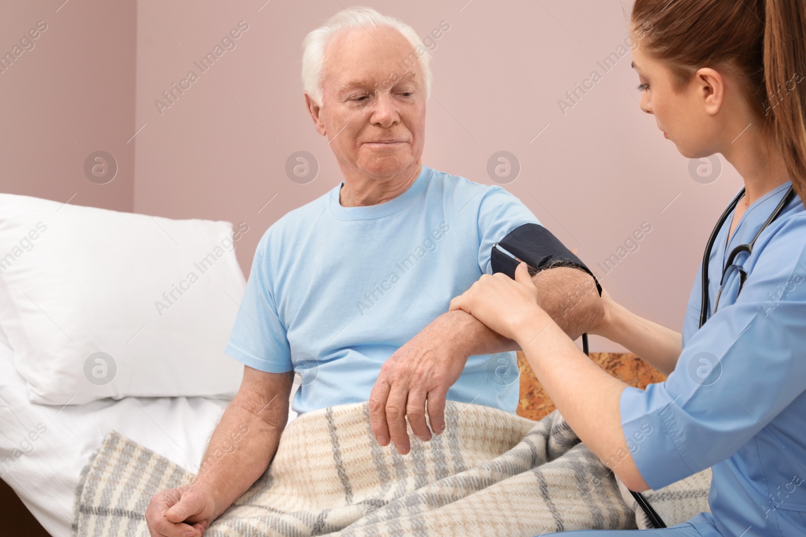 Photo of Nurse measuring senior man's blood pressure in hospital ward. Medical assisting