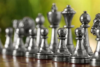 Photo of Silver chess pieces on game board against blurred background, closeup