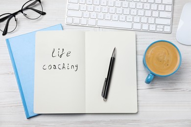 Phrase Life Coaching written in notebook, pen, cup of coffee, glasses and keyboard on white wooden table, flat lay