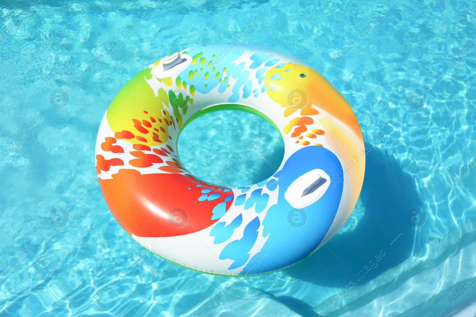 Photo of Colorful inflatable ring floating in swimming pool on sunny day, outdoors