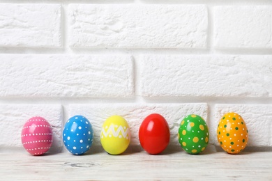 Decorated Easter eggs on table near brick wall. Space for text