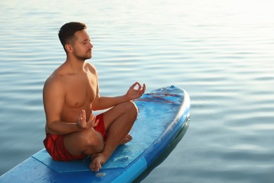 Man meditating on light blue SUP board on river at sunset