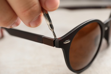 Handyman repairing sunglasses with screwdriver at grey table, closeup