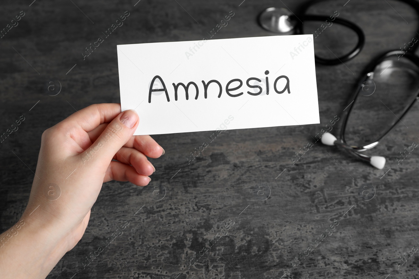 Photo of Woman holding card with word Amnesia at grey table, closeup