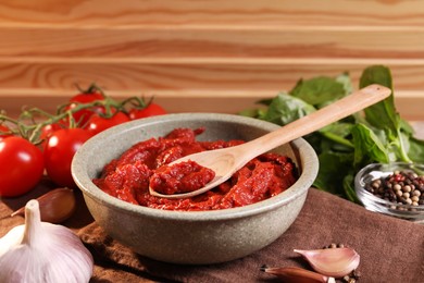 Photo of Bowl of tasty tomato paste with spoon and ingredients on table