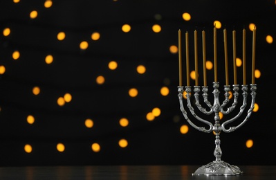Photo of Hanukkah menorah with candles on table against blurred lights