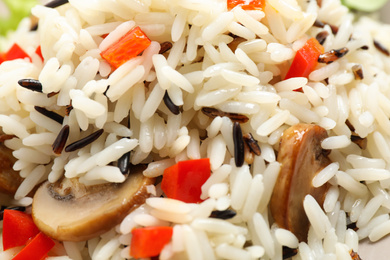 Delicious rice pilaf with bell peppers and mushrooms as background, closeup